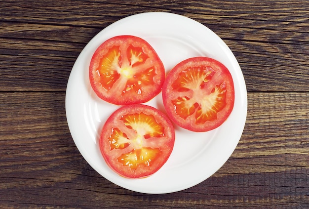 Tranches de tomates mûres dans une assiette sur une table en bois sombre, vue de dessus