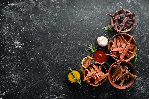 Tranches de viande séchée séchée avec des épices et des herbes Des collations pour la bière Sur un fond de pierre noire Vue de dessus