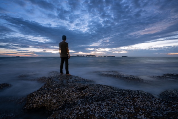 Tranquille baie pierreuse avec un arrière de l'homme après le coucher du soleil.