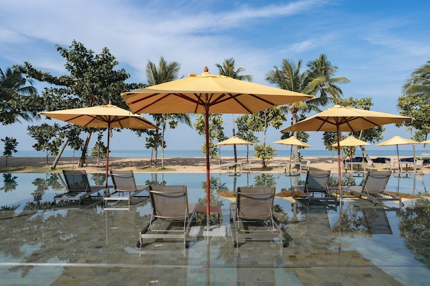 Transats avec parasol jaune dans la piscine de l'hôtel tropical près de la plage.