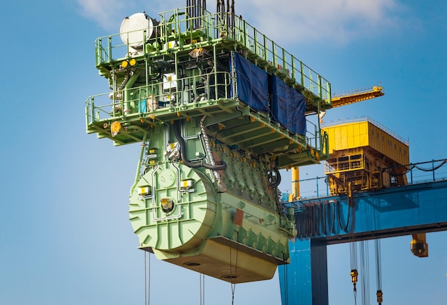 Transport d'un gros moteur marin par une grue portuaire à l'aide de câbles en acier