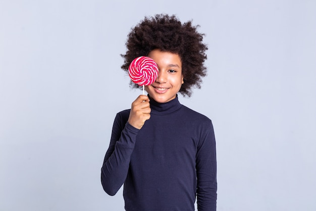 Transportant des bonbons colorés. Rayonnant un jeune homme bouclé fermant son visage avec des bonbons rouges sucrés tout en posant pour des caméramans