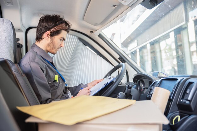 Transporteur avec uniforme dans le siège du conducteur regardant les colis pour livrer les commandes