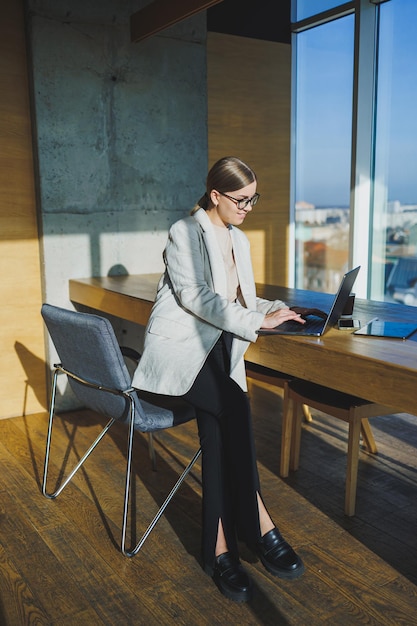 Travail de bureau séduisante jeune femme gestionnaire travaillant au bureau debout dans un espace de travail lumineux à l'aide d'un ordinateur portable moderne jeune fille ayant un appel vidéo via un ordinateur portable