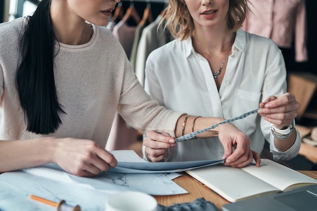 Travail sur des designs tendance. Gros plan sur des jeunes femmes travaillant sur des échantillons assis dans l'atelier