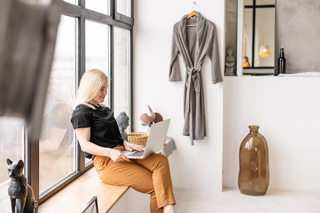 Travail à distance à domicile, indépendant pendant la quarantaine covid-19. Dame souriante assise et travaillant sur un ordinateur portable dans un intérieur confortable de salon, espace libre.