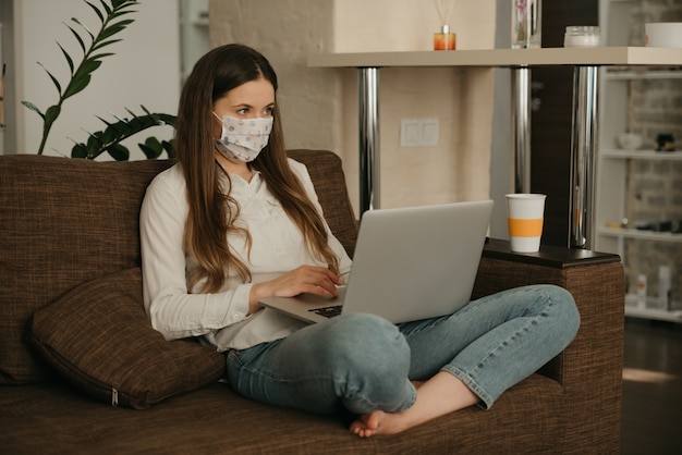 Travail à distance. Femme dans un masque médical étudiant à distance sur son ordinateur portable pendant la quarantaine