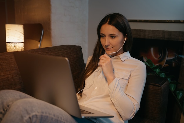 Travail à distance. Une femme de race blanche avec des écouteurs travaillant à distance sur son ordinateur portable. Une femme d'affaires faisant une vidéoconférence assis sur le canapé.