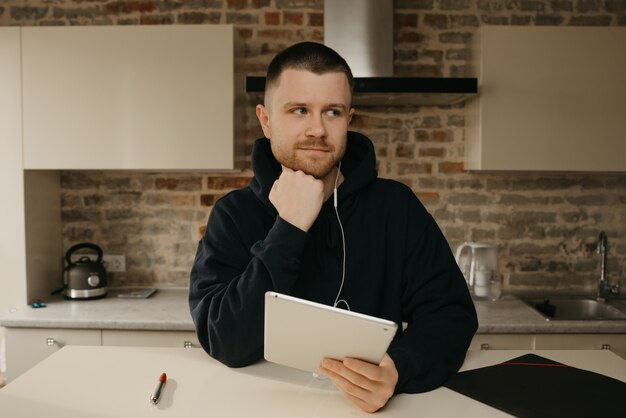 Travail à distance. Un homme avec une barbe travaillant à distance sur sa tablette. Un programmeur entendant un webinaire.