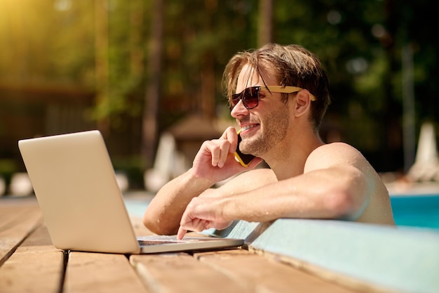 Travail à distance. Jeune homme à la piscine travaillant sur un ordinateur portable