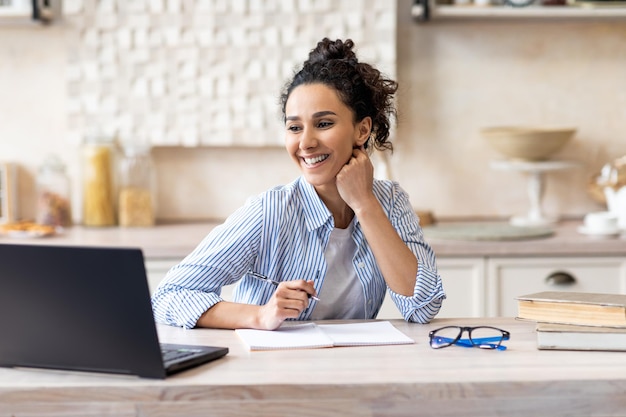 Travail à domicile femme pigiste heureuse travaillant sur un ordinateur portable à l'intérieur de la cuisine bénéficiant d'un travail à distance