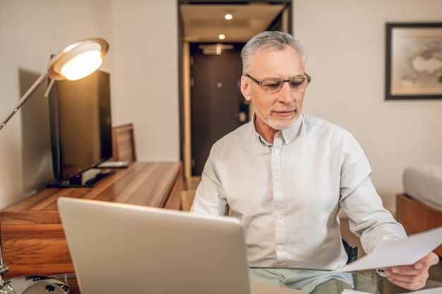 Travail à domicile. Homme aux cheveux gris à lunettes travaillant sur un ordinateur portable et ayant l'air sérieux