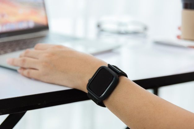 Travail à domicile, une jeune femme d'affaires asiatique heureuse utilise un ordinateur portable moderne à écran tactile, elle porte une montre intelligente au poignet, se concentre sur la montre intelligente