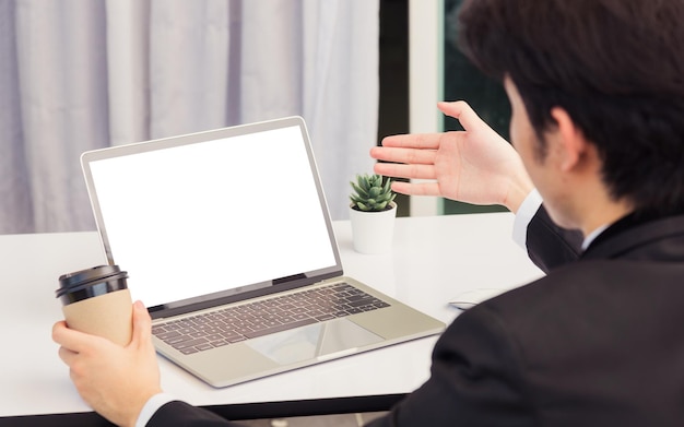 Travail à domicile, un jeune homme d'affaires asiatique sourit en costume vidéoconférence ou facetime par ordinateur portable lève la main pour expliquer à ses coéquipiers sur le bureau à la maison