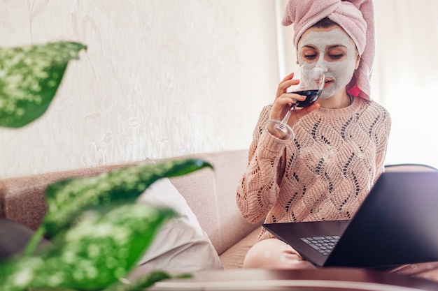 Travail à domicile pendant la quarantaine des coronavirus. Femme avec masque facial appliqué à boire du vin à l'aide d'un ordinateur portable sur le verrouillage