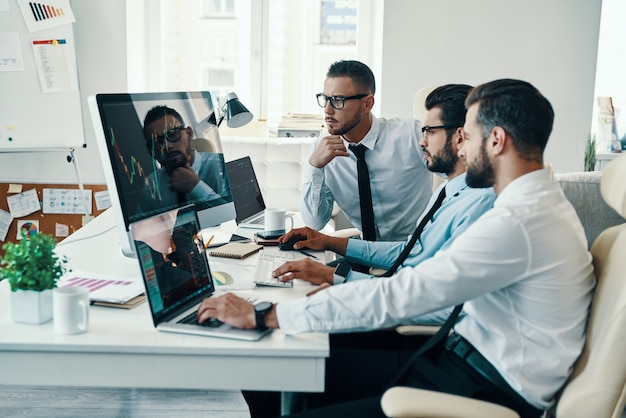 Travail en équipe. Groupe de jeunes hommes modernes en tenue de soirée analysant les données boursières tout en travaillant au bureau