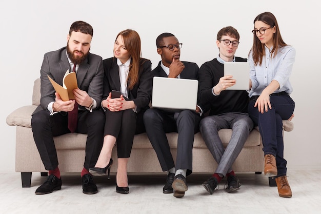 Travail en équipe. Jeunes hommes d'affaires multiethniques avec des appareils discutant d'une nouvelle stratégie marketing, assis sur un canapé dans un bureau moderne, espace de copie