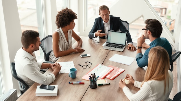 Travail d'équipe sérieux homme mûr en tenue de soirée montrant quelque chose sur la tablette numérique et discutant