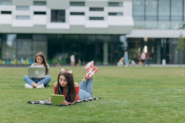 Travail en freelance. Apprentissage des élèves. Deux jolies filles amis assis sur l'herbe verte.