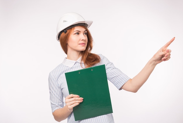 Travail, ingénierie, concept de personnes - Jeune belle femme rousse en casque d'architecte avec des documents montrant un nouveau projet.