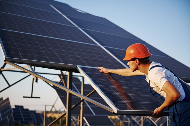 Travail manuel. Travailleur masculin en uniforme bleu à l'extérieur avec des batteries solaires aux beaux jours.