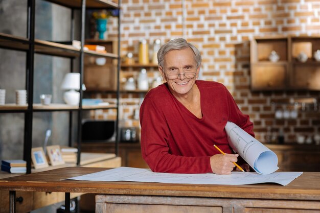 Travail préféré. Enthousiaste homme âgé ravi holing son plan et souriant tout en appréciant son travail