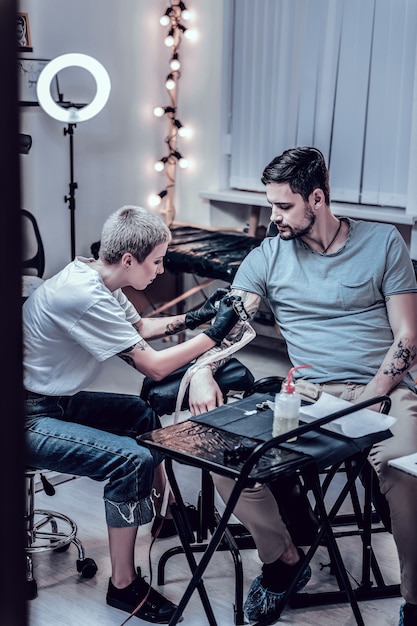 Travail de tatouage inachevé. Maître attentif et sa session de dépenses client obéissante dans un salon de tatouage tout en terminant le dernier travail