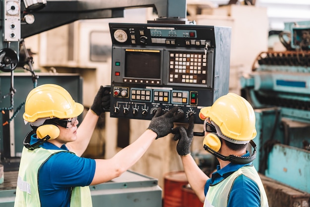 Travail à l'usine. Un travailleur asiatique travaillant dans des vêtements de travail de sécurité avec un casque jaune et un casque antibruit à l'aide d'équipement.