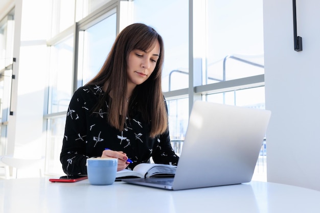 Travaillant dans un café, une brune écrit dans un journal et regarde un moniteur d'ordinateur portableTravail à distance pas au bureau