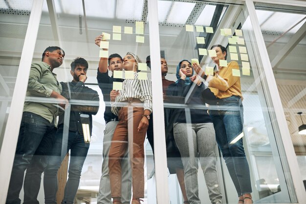 Travaillant sur leurs meilleurs concepts Photo d'un groupe d'hommes d'affaires en train de réfléchir avec des notes sur un mur de verre dans un bureau