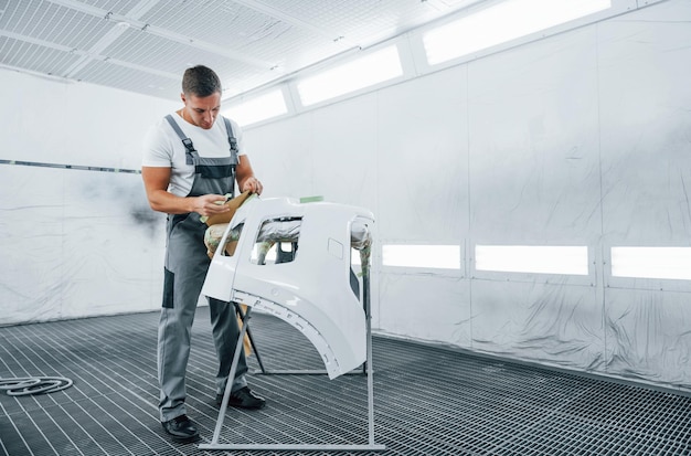 Travaille avec un capot de voiture Réparateur automobile caucasien en uniforme dans un garage