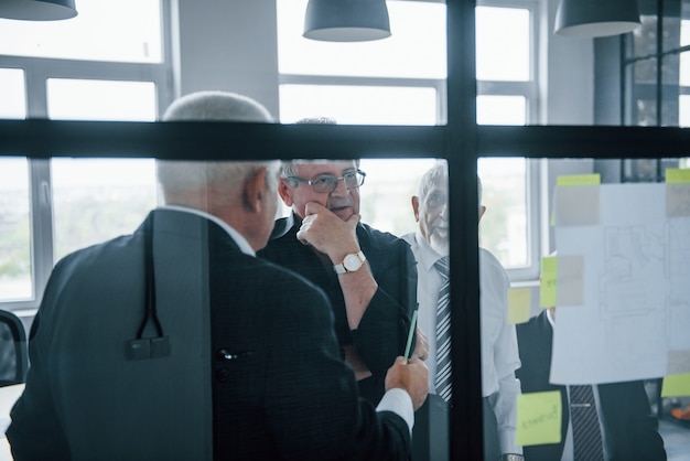 Travailler avec des autocollants sur verre. Une équipe âgée d'architectes d'affaires âgés a une réunion au bureau.