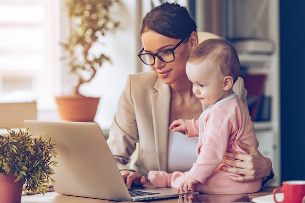 Travailler ensemble. Jeune belle femme d'affaires utilisant un ordinateur portable alors qu'elle était assise avec sa petite fille sur son lieu de travail