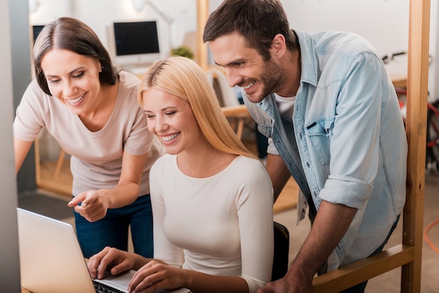 Travailler ensemble sur un projet. Trois hommes d'affaires joyeux dans des vêtements décontractés intelligents regardant l'ordinateur portable ensemble et souriant