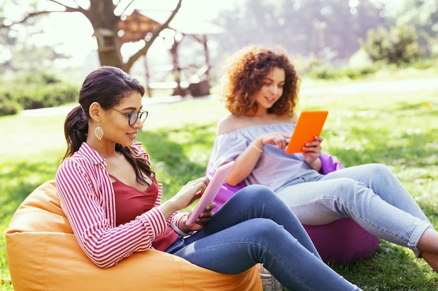 Travailler à l'extérieur. Enthousiaste femme brune assise dans la chaise et travaillant sur sa tablette