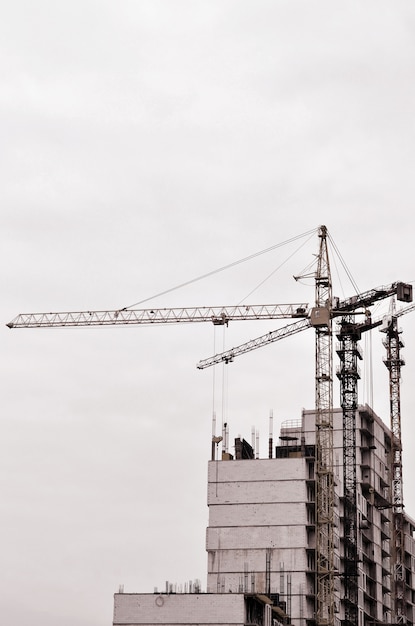 Travailler De Hautes Grues à L'intérieur Pour Les Grands Immeubles En Construction Contre Un Ciel Bleu Clair.