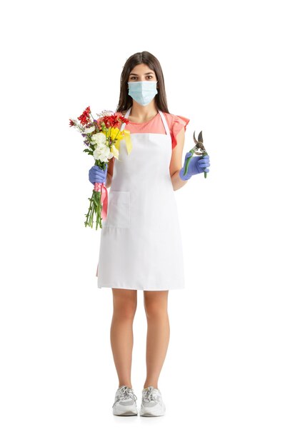 Travailler en masque facial. Belle jeune femme, fleuriste avec bouquet frais coloré isolé sur fond de studio blanc. Femme de race blanche, travailleur de l'art moderne. Finance, économie, profession libérale.