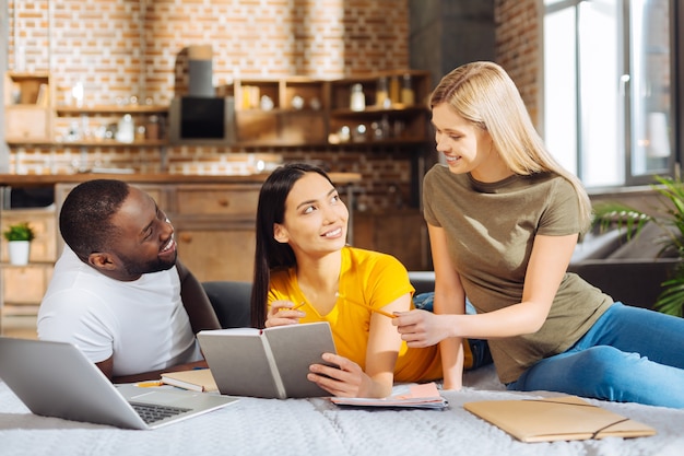 Travailler sur une tâche. Trois étudiants agréables et joyeux qui étudient et rient alors que la belle femme montre l'erreur