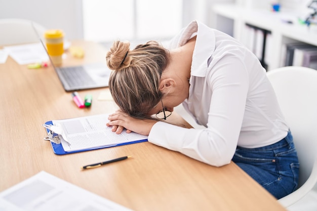 Travailleur d'affaires de jeune femme blonde a souligné avec la tête sur la table au bureau