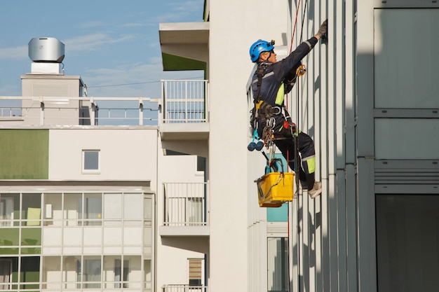 Un travailleur d'alpinisme industriel est suspendu au-dessus d'un immeuble résidentiel tout en lavant le vitrage de la façade extérieure