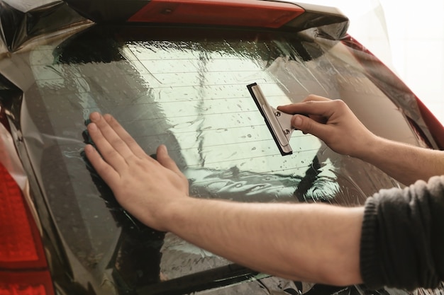 Travailleur appliquant une feuille de teinture sur la fenêtre de la voiture