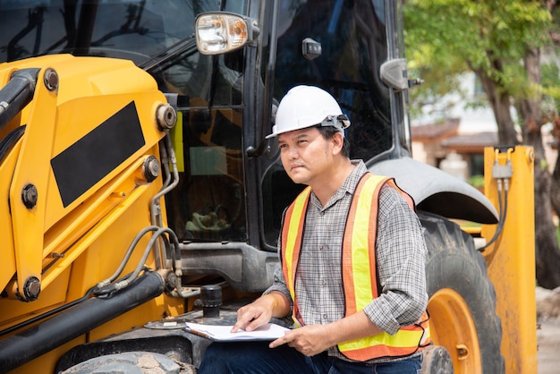 Travailleur ou architecte d'ingénieur en construction civile asiatique avec casque et gilet de sécurité travaillant et tenant une note de carton pour voir des plans ou un plan sur un bâtiment ou un chantier de construction