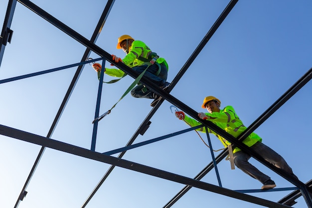 Un travailleur asiatique porte un équipement de hauteur de sécurité pour construire une structure de toit en acier sur le chantier de construction.