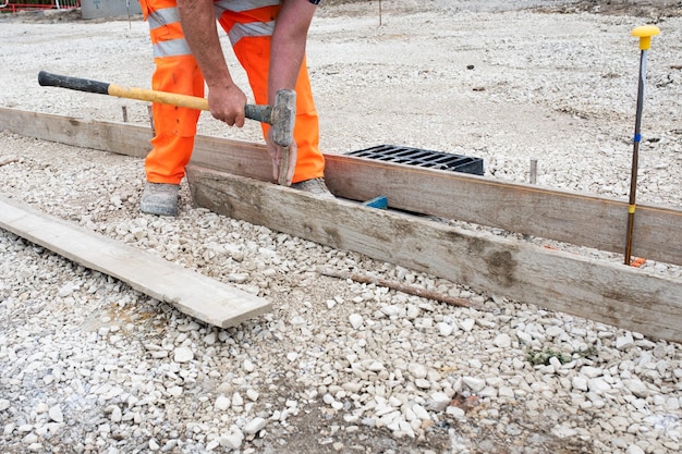 Travailleur au sol faisant l'obturateur pour le béton pour former une base pour la bordure à l'aide de planches d'échafaudage