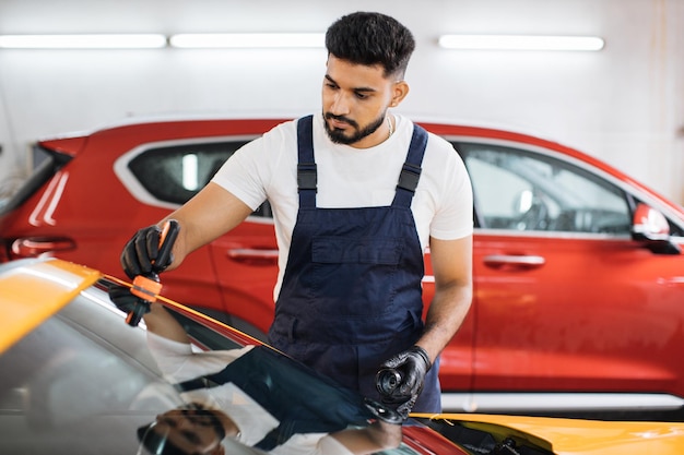 Travailleur barbu masculin en salopette bleue et gants de protection sur un service de lavage de voiture professionnel