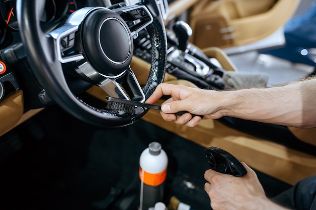 Travailleur avec brosse essuie le volant de voiture, nettoyage à sec et détails