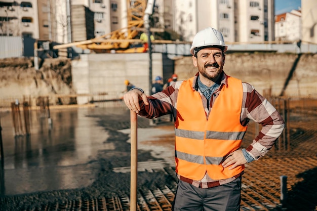 Un travailleur de chantier heureux s'appuie sur une pelle et sourit à la caméra sur place