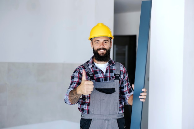 Un travailleur de chantier souriant et heureux se tient dans un nouveau bâtiment avec une poutre métallique à la main