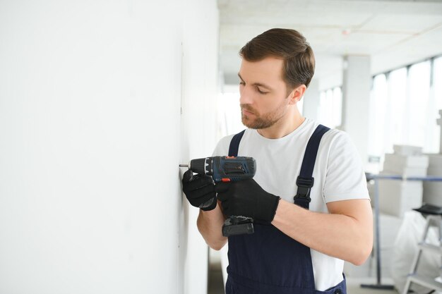 Le travailleur de cloisons sèches travaille sur le chantier dans une maison