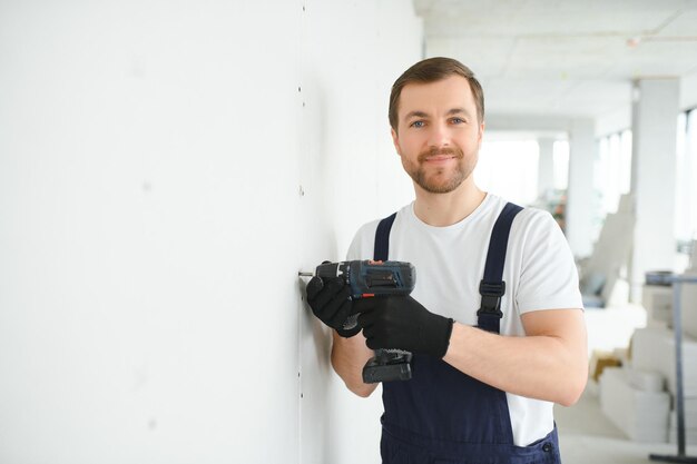 Le travailleur de cloisons sèches travaille sur le chantier dans une maison